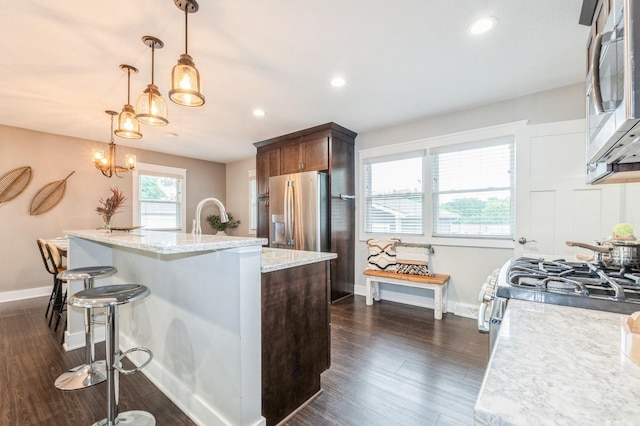 3817 80th St, Urbandale, IA 50322 - kitchen with stainless steel appliances, dark wood finished floors, a kitchen island with sink, a breakfast bar area, and light stone counters