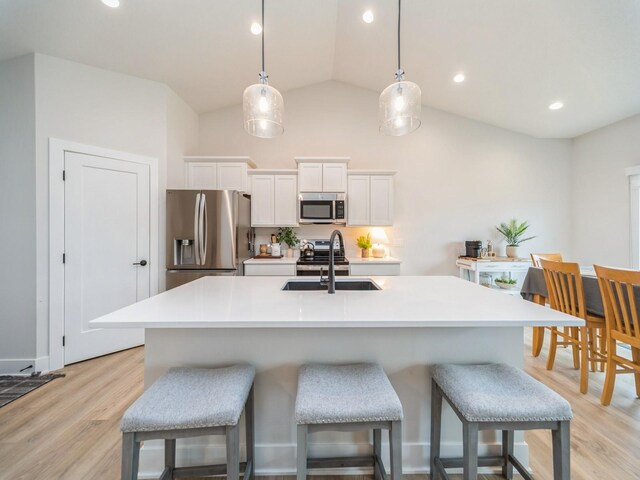 645 NW Prairie Rose Ln, Waukee, IA 50263 - kitchen with stainless steel appliances, a breakfast bar, white cabinetry, light wood-style flooring, and a center island with sink