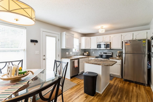 276 NW Georgetown Blvd, Ankeny, IA 50023 - kitchen featuring appliances with stainless steel finishes, backsplash, white cabinets, wood finished floors, and a kitchen island