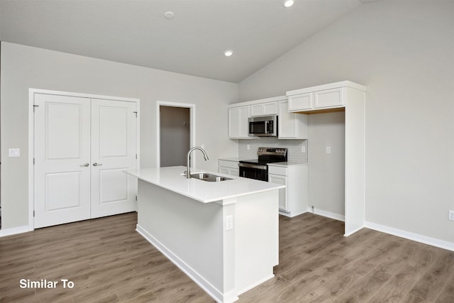 1163 NW Petersen Dr, Waukee, IA 50263 - kitchen featuring stainless steel appliances, white cabinets, light wood-style floors, an island with sink, and vaulted ceiling