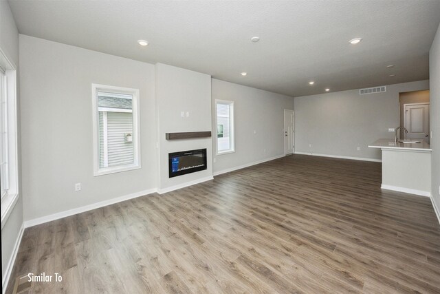 9764 Regatta Ln, Johnston, IA 50131 - unfurnished living room with wood finished floors, a glass covered fireplace, and recessed lighting