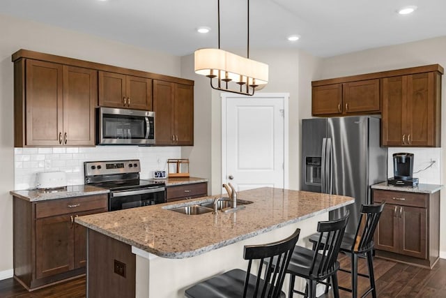 210 SE Willow Run Ln, Ankeny, IA 50021 - kitchen featuring appliances with stainless steel finishes, dark wood finished floors, a breakfast bar, decorative backsplash, and light stone counters