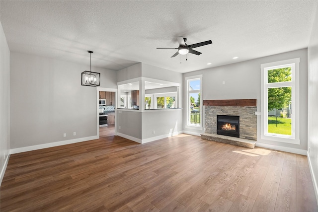 1217 NW Morningside Ct, Grimes, IA 50111 - unfurnished living room with a ceiling fan, a textured ceiling, wood finished floors, healthy amount of natural light, and a stone fireplace