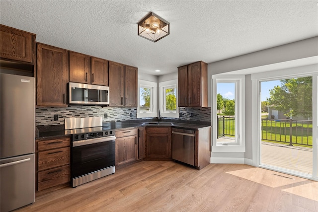 1217 NW Morningside Ct, Grimes, IA 50111 - kitchen featuring stainless steel appliances, dark countertops, light wood-style floors, decorative backsplash, and a textured ceiling