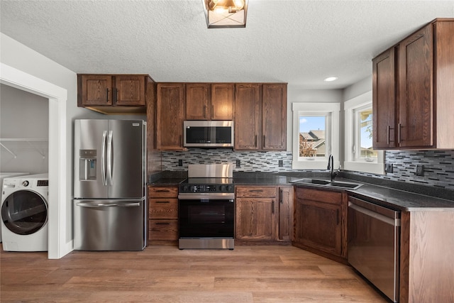 1217 NW Morningside Ct, Grimes, IA 50111 - kitchen featuring appliances with stainless steel finishes, washer / dryer, dark countertops, light wood-style flooring, and a textured ceiling