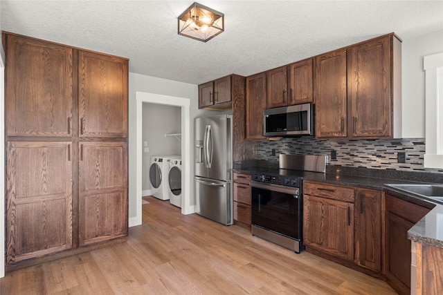 1217 NW Morningside Ct, Grimes, IA 50111 - kitchen featuring stainless steel appliances, washing machine and dryer, light wood-style flooring, tasteful backsplash, and a textured ceiling