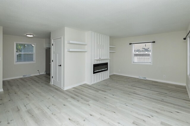 3113 E 36th Ct, Des Moines, IA 50317 - unfurnished living room featuring light wood finished floors, plenty of natural light, and a glass covered fireplace