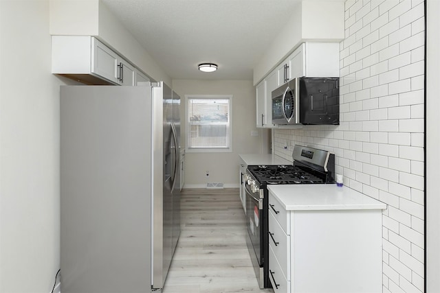 3113 E 36th Ct, Des Moines, IA 50317 - kitchen featuring appliances with stainless steel finishes, light wood-style flooring, light countertops, white cabinets, and tasteful backsplash