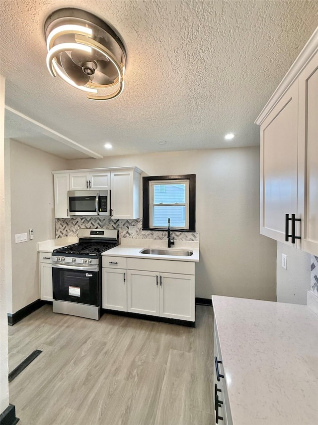 1254 E 16th St, Des Moines, IA 50316 - kitchen featuring appliances with stainless steel finishes, a textured ceiling, light wood finished floors, light countertops, and tasteful backsplash
