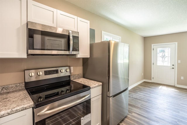 2311 Williams St, Des Moines, IA 50317 - kitchen with appliances with stainless steel finishes, light wood finished floors, white cabinets, a textured ceiling, and light stone countertops