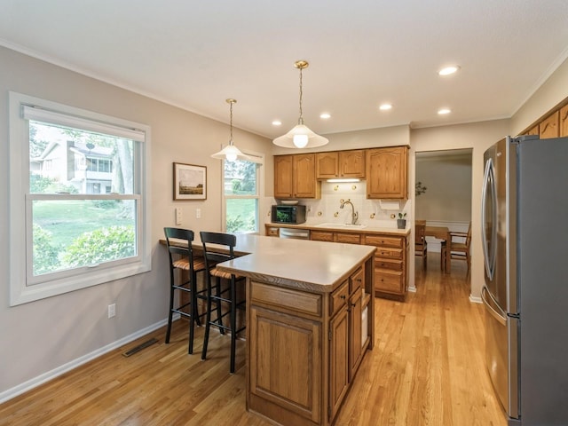 2906 Watrous Ave, Des Moines, IA 50321 - kitchen featuring stainless steel appliances, brown cabinets, light wood-type flooring, ornamental molding, and healthy amount of natural light
