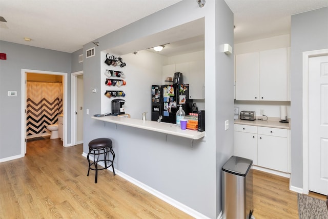 2323 E Porter Ave Unit 36, Des Moines, IA 50320 - kitchen featuring black fridge with ice dispenser, a kitchen bar, light wood-style flooring, and white cabinetry