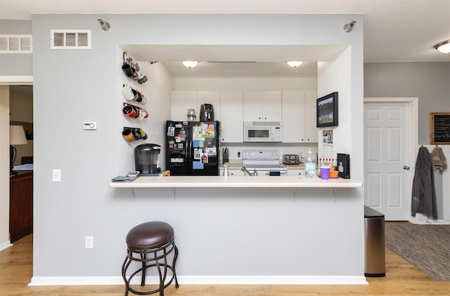 2323 E Porter Ave Unit 36, Des Moines, IA 50320 - kitchen with white appliances, a peninsula, light wood-type flooring, and a breakfast bar