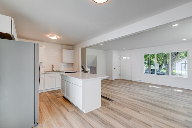 4132 E 24th Ct, Des Moines, IA 50317 - kitchen featuring freestanding refrigerator, white cabinets, light wood finished floors, tasteful backsplash, and light countertops