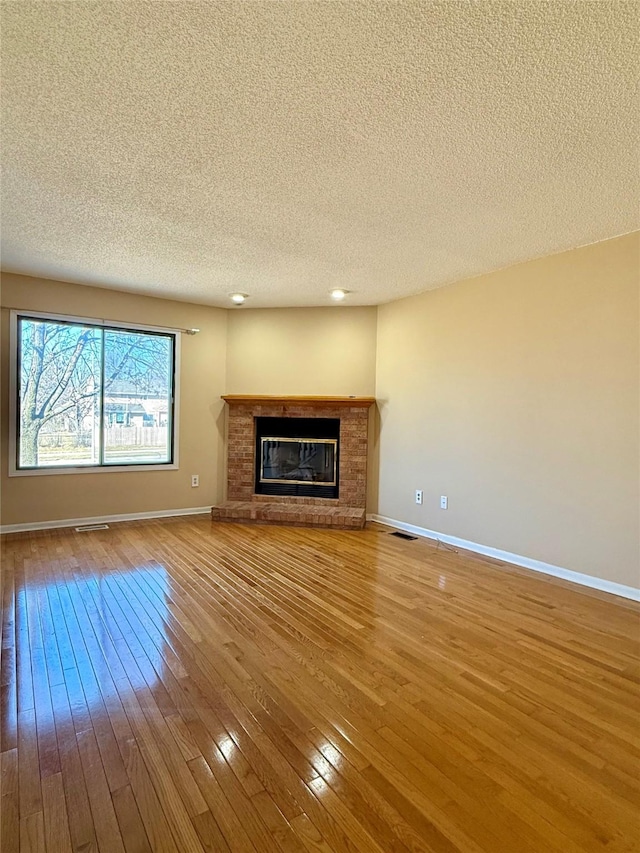 2519 W 1st St, Ankeny, IA 50023 - unfurnished living room featuring wood-type flooring, a textured ceiling, and a brick fireplace