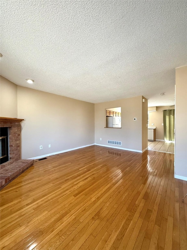 2519 W 1st St, Ankeny, IA 50023 - unfurnished living room featuring a textured ceiling, light wood-style flooring, and a brick fireplace