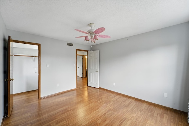 1228 64th St, West Des Moines, IA 50266 - unfurnished bedroom featuring light wood finished floors, a walk in closet, a textured ceiling, a closet, and ceiling fan