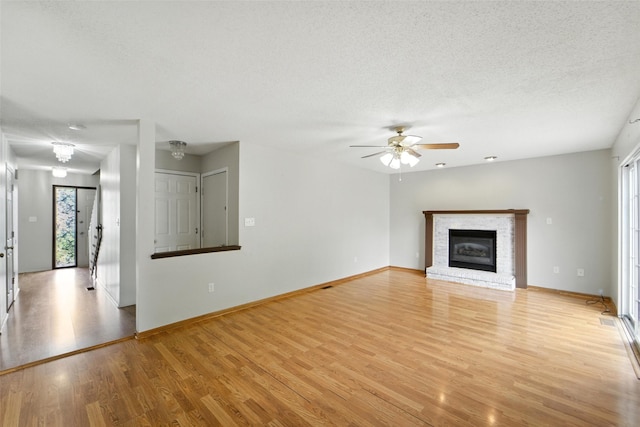 1228 64th St, West Des Moines, IA 50266 - unfurnished living room featuring light wood-type flooring, healthy amount of natural light, ceiling fan, a brick fireplace, and a textured ceiling