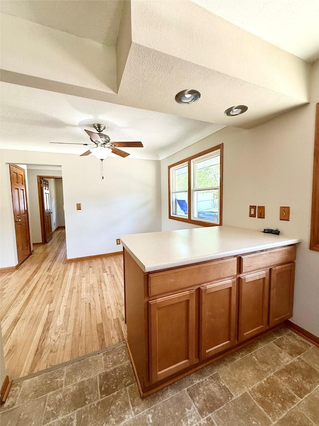 3355 Kinsey Ave, Des Moines, IA 50317 - kitchen featuring a textured ceiling, brown cabinets, a peninsula, stone tile floors, and ceiling fan