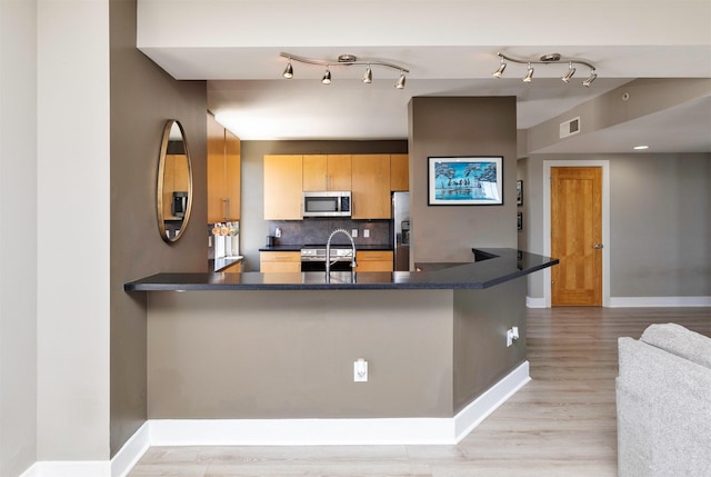 400 Walnut St Unit 901, Des Moines, IA 50309 - kitchen featuring stainless steel appliances, dark countertops, light wood finished floors, a peninsula, and tasteful backsplash
