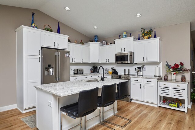 690 SE Driftwood Ln, Waukee, IA 50263 - kitchen featuring stainless steel appliances, vaulted ceiling, white cabinets, light wood finished floors, and light stone counters