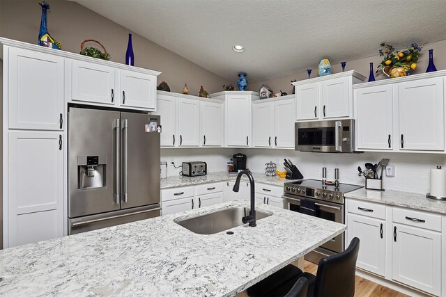 690 SE Driftwood Ln, Waukee, IA 50263 - kitchen with appliances with stainless steel finishes, white cabinetry, vaulted ceiling, light stone counters, and decorative backsplash