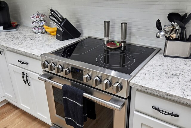 690 SE Driftwood Ln, Waukee, IA 50263 - kitchen with stainless steel range with electric stovetop, decorative backsplash, white cabinetry, light stone countertops, and light wood-style floors