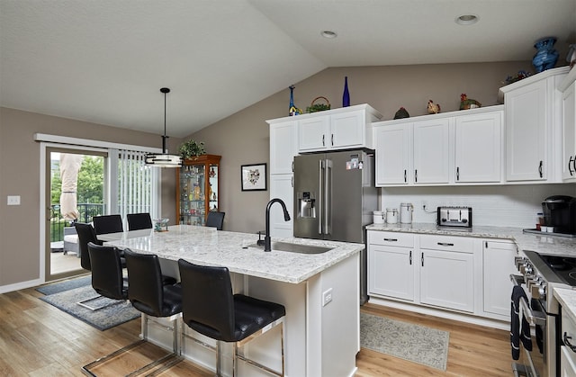 690 SE Driftwood Ln, Waukee, IA 50263 - kitchen featuring appliances with stainless steel finishes, vaulted ceiling, light wood finished floors, white cabinets, and light stone counters