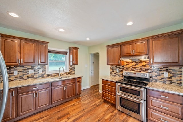 2560 E Sheridan Ave, Des Moines, IA 50317 - kitchen with double oven range, under cabinet range hood, light wood-style flooring, recessed lighting, and decorative backsplash