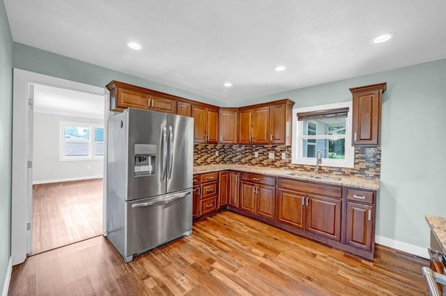 2560 E Sheridan Ave, Des Moines, IA 50317 - kitchen with stainless steel fridge with ice dispenser, light wood-style flooring, decorative backsplash, brown cabinetry, and light stone countertops