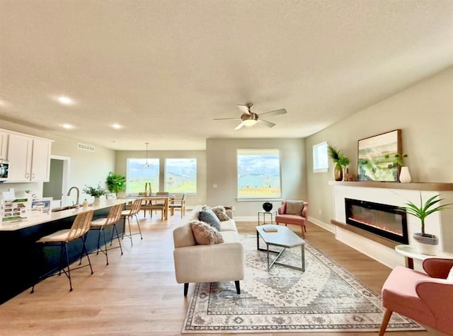 5610 Leyden Ave, Des Moines, IA 50317 - living area with light wood-type flooring, a glass covered fireplace, recessed lighting, and a ceiling fan