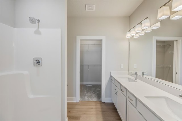 5610 Leyden Ave, Des Moines, IA 50317 - bathroom featuring wood finished floors, double vanity, a walk in closet, and a shower