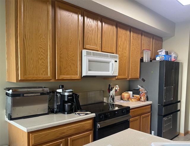 2101 Meadow Ct Unit 304, Des Moines, IA 50320 - kitchen with white microwave, black electric range oven, light countertops, freestanding refrigerator, and brown cabinetry