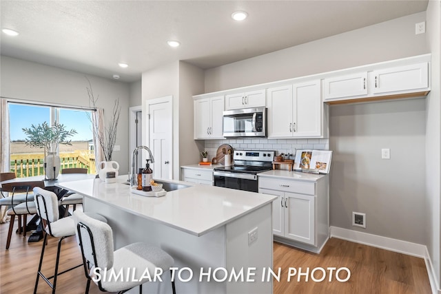 1488 S 91st St, West Des Moines, IA 50266 - kitchen featuring appliances with stainless steel finishes, white cabinetry, backsplash, a center island with sink, and light wood-type flooring