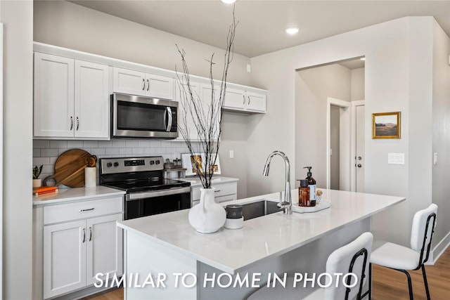 1488 S 91st St, West Des Moines, IA 50266 - kitchen with stainless steel appliances, white cabinetry, decorative backsplash, a center island with sink, and light countertops