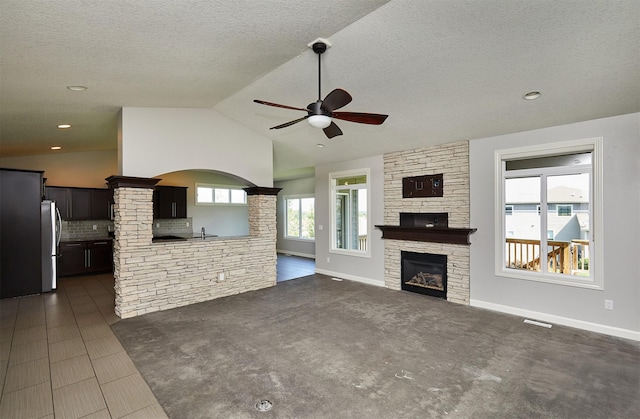 9305 Sugar Creek Cir, West Des Moines, IA 50266 - unfurnished living room featuring ceiling fan, a stone fireplace, lofted ceiling, and a textured ceiling