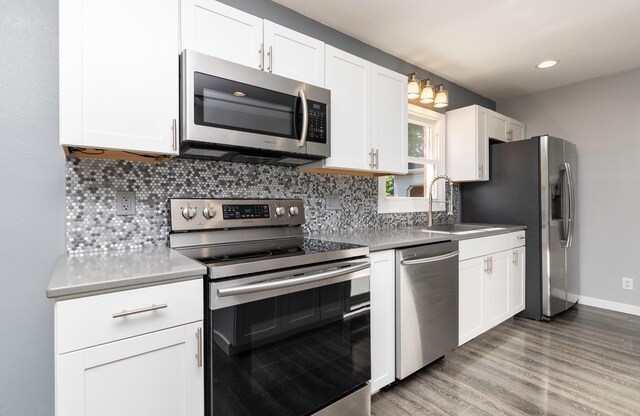 1808 Payton Ave, Des Moines, IA 50315 - kitchen with appliances with stainless steel finishes, backsplash, white cabinetry, wood finished floors, and light countertops