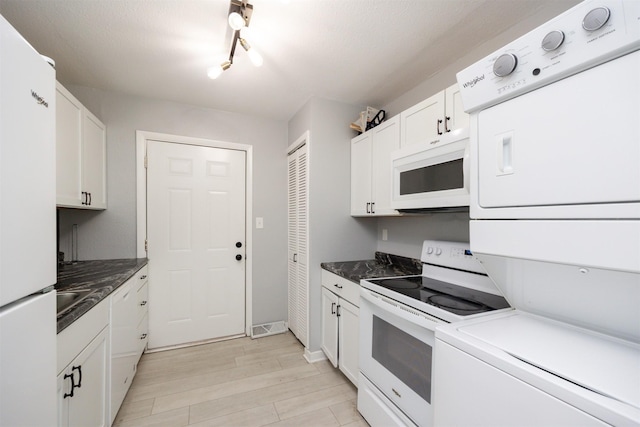 3416 Garfield Ave, Des Moines, IA 50317 - kitchen with white appliances, stacked washer and clothes dryer, light wood finished floors, white cabinets, and dark countertops
