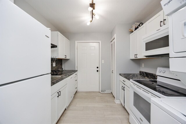 3416 Garfield Ave, Des Moines, IA 50317 - kitchen featuring white appliances, dark countertops, white cabinets, estacked washer and dryer, and light wood-style floors