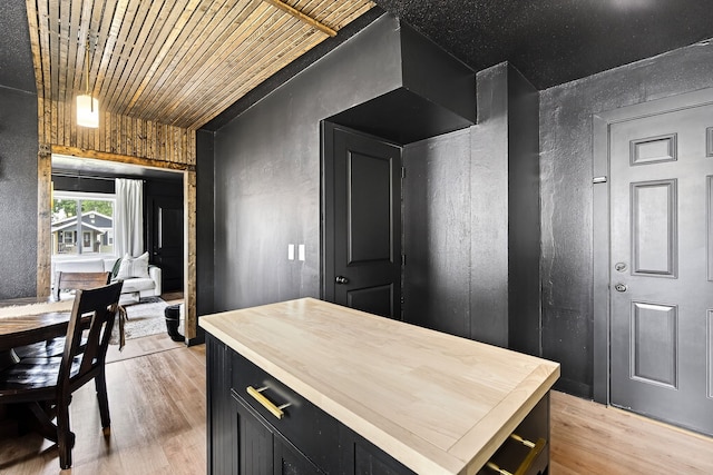 1315 Bundy St, Des Moines, IA 50315 - kitchen with dark cabinets, butcher block countertops, light wood finished floors, a textured wall, and a center island