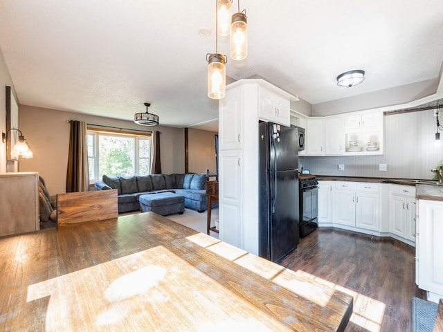 808 SW 2nd St, Stuart, IA 50250 - kitchen with black appliances, dark wood-style floors, white cabinetry, open floor plan, and decorative light fixtures