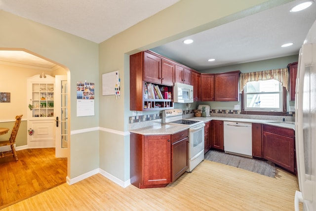 1209 Edgemont St, Des Moines, IA 50315 - kitchen featuring white appliances, light wood-style flooring, reddish brown cabinets, arched walkways, and recessed lighting