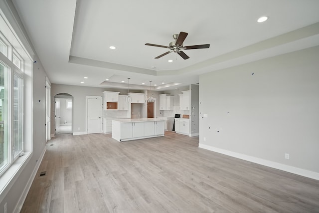 45 NW Alderleaf Dr, Waukee, IA 50263 - unfurnished living room with arched walkways, a ceiling fan, recessed lighting, a raised ceiling, and light wood-type flooring