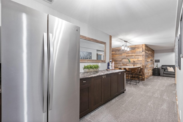 54 Four Winds Dr, Clear Lake, IA 50428 - kitchen featuring freestanding refrigerator, wooden walls, light carpet, dark brown cabinets, and light stone countertops