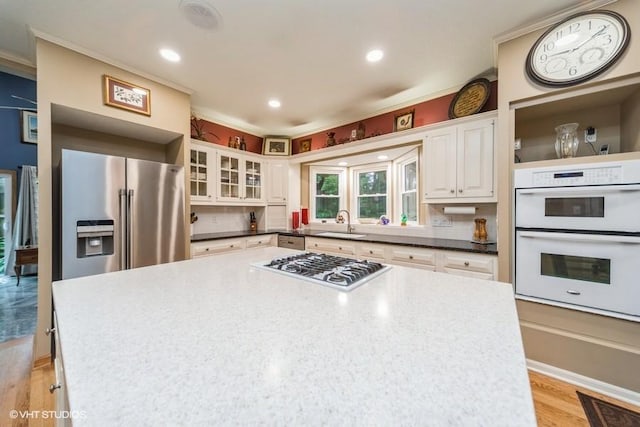 7100 Holcomb Ave, Urbandale, IA 50322 - kitchen featuring stainless steel fridge with ice dispenser, gas cooktop, light wood finished floors, white cabinets, and white double oven