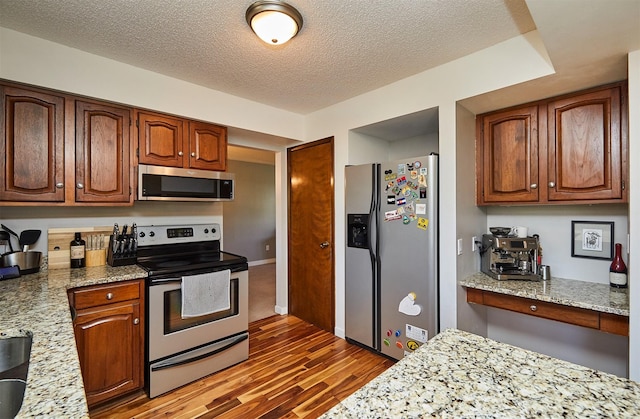 5208 Pommel Pl, West Des Moines, IA 50265 - kitchen featuring stainless steel appliances, wood finished floors, a textured ceiling, light stone countertops, and brown cabinetry