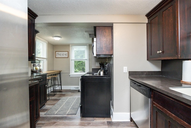 951 28th St, Des Moines, IA 50312 - kitchen with stainless steel dishwasher, a textured ceiling, light wood-type flooring, stove, and dark countertops