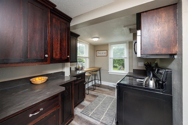 951 28th St, Des Moines, IA 50312 - kitchen featuring black range with electric stovetop, a textured ceiling, dark countertops, light wood-style floors, and stainless steel microwave