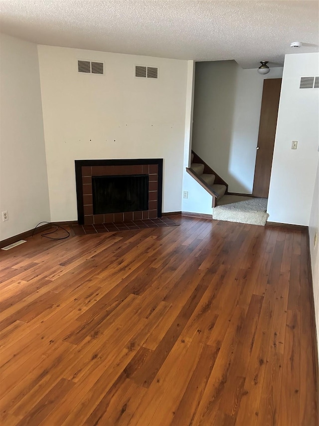 937 15th St NE, Newton, IA 50208 - unfurnished living room featuring wood-type flooring, a fireplace with flush hearth, stairway, and a textured ceiling