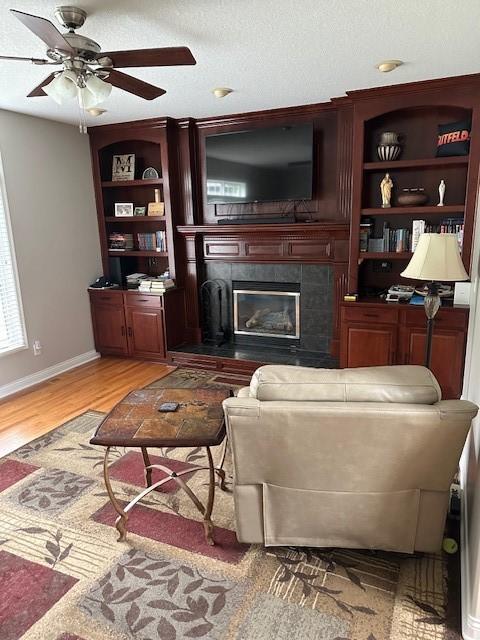 4017 160th St, Urbandale, IA 50323 - living room featuring a tiled fireplace, light wood-style floors, a ceiling fan, and built in shelves